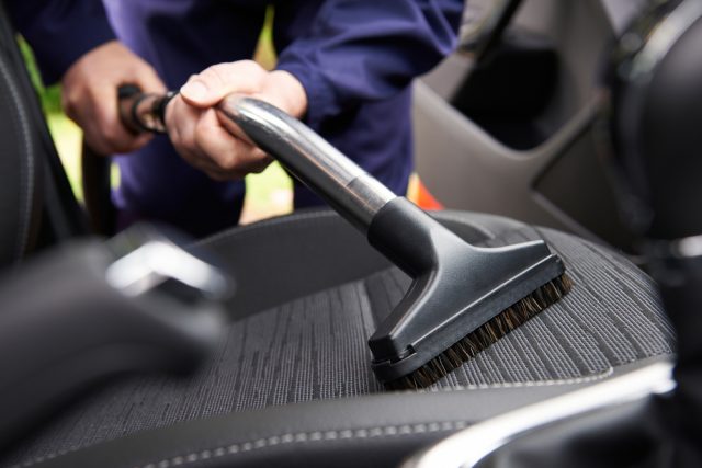 Man hoovering passenger seat of a car