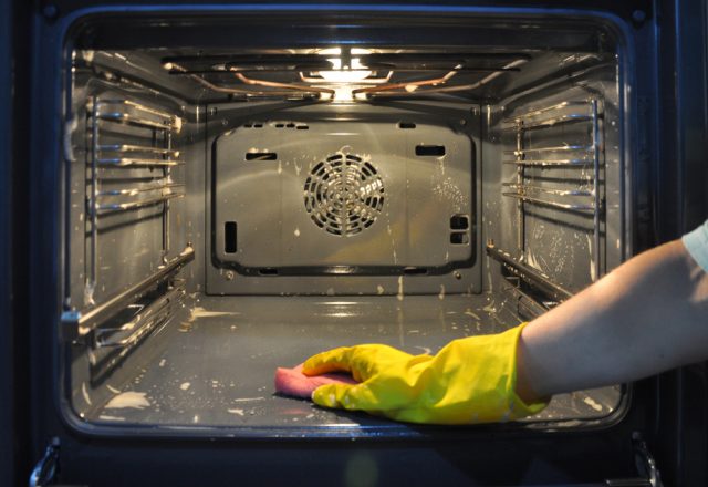 Man with yellow rubber gloves scrubbing the inside of an oven