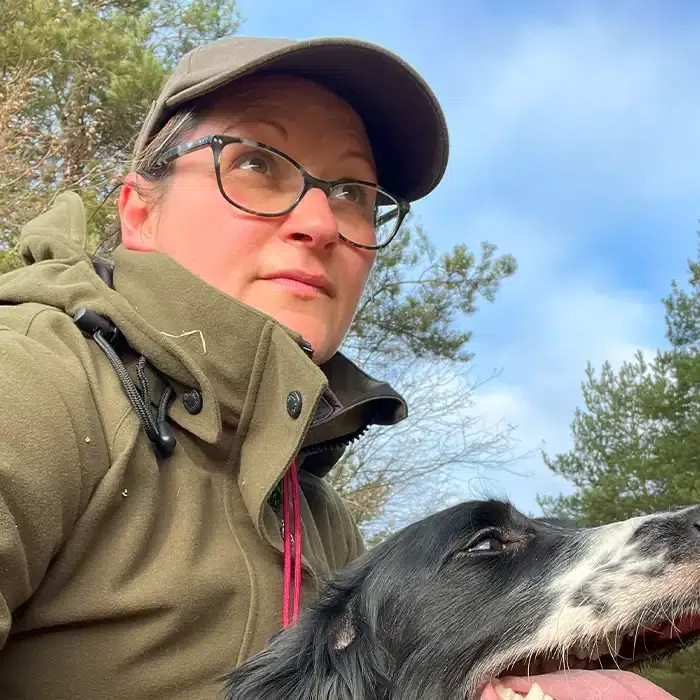 Mel Newton outdoors during a dog training session in Norfolk, holding a black and white dog.