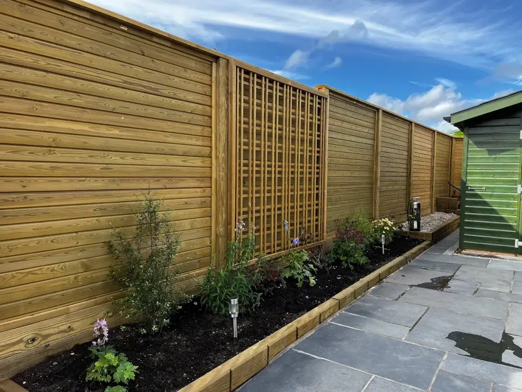 Timber garden fencing and trellis installed beside a landscaped flower bed and paved patio